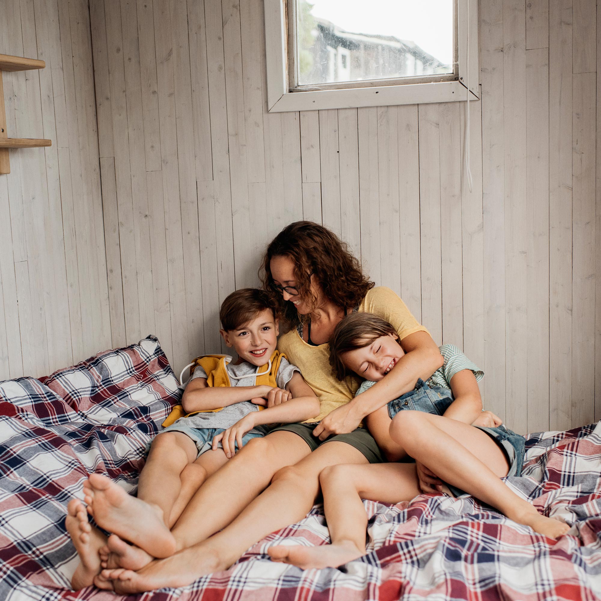 Mamma och två barn sitter på en säng och kramas