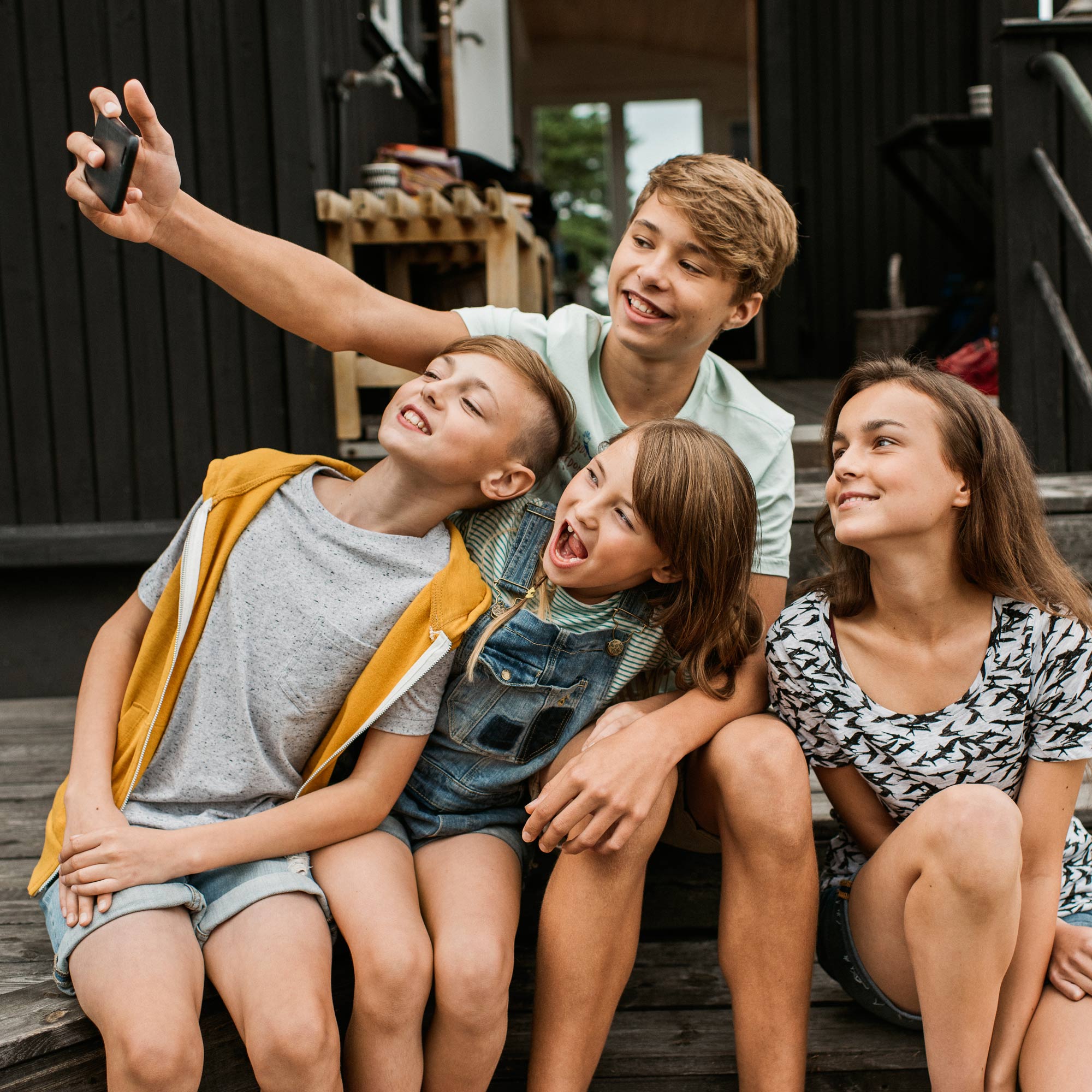 Fyra barn tar en gruppbild med en mobil ute på en terrass