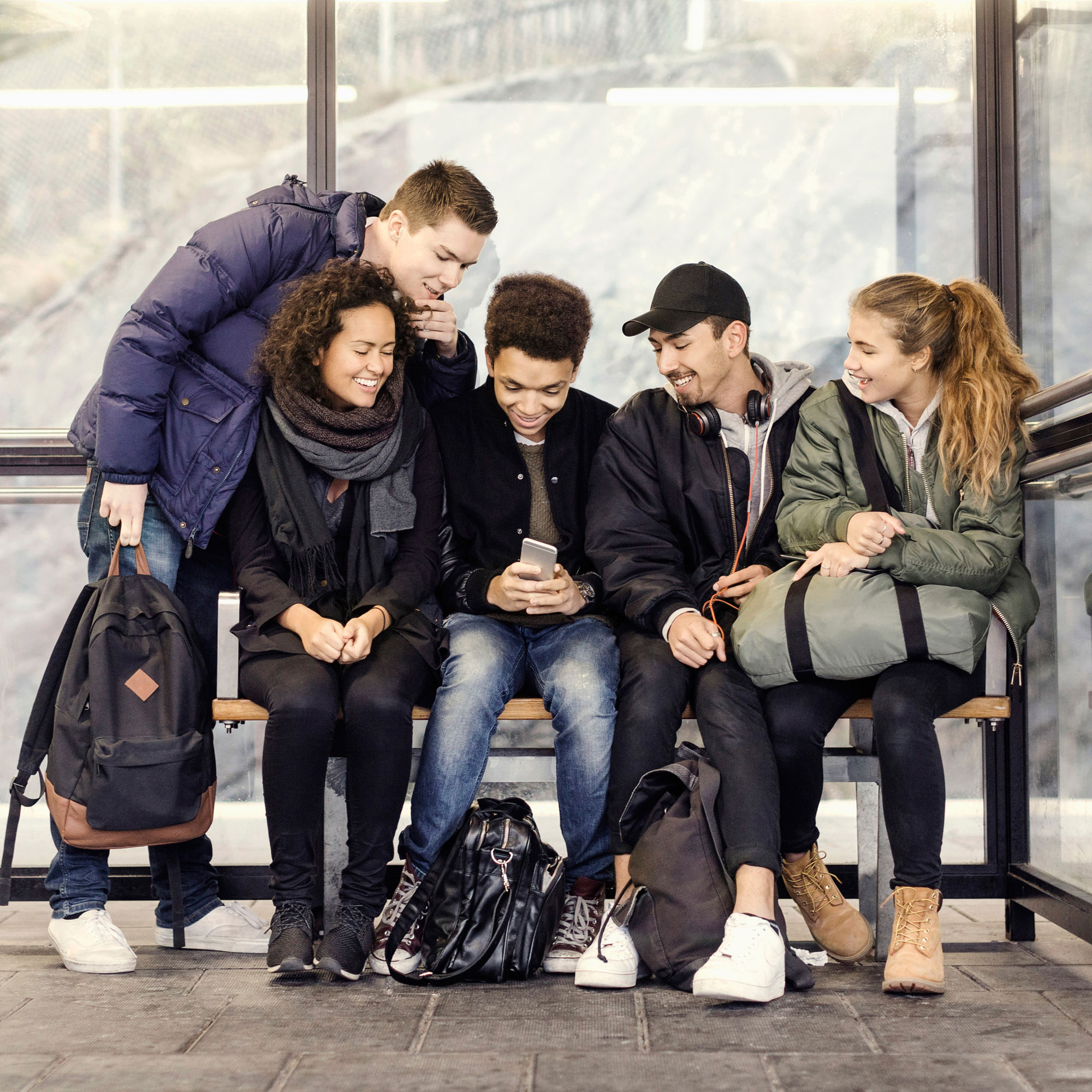 Ungdomar sitter och väntar på bussen och tittar på en mobil